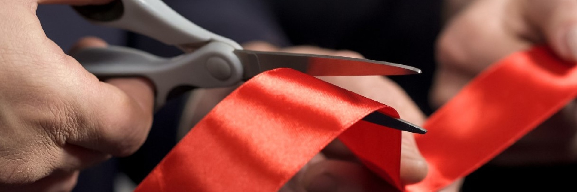 image of a hand with scissors cutting a ribbon