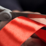 image of a hand with scissors cutting a ribbon